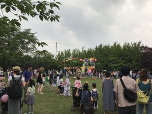 芝生広場中央に設けたやぐらを囲むように、お馴染みの音楽で盆踊りを楽しむ様子です。300人前後の参加者が集まり、子ども達が列を作っています。