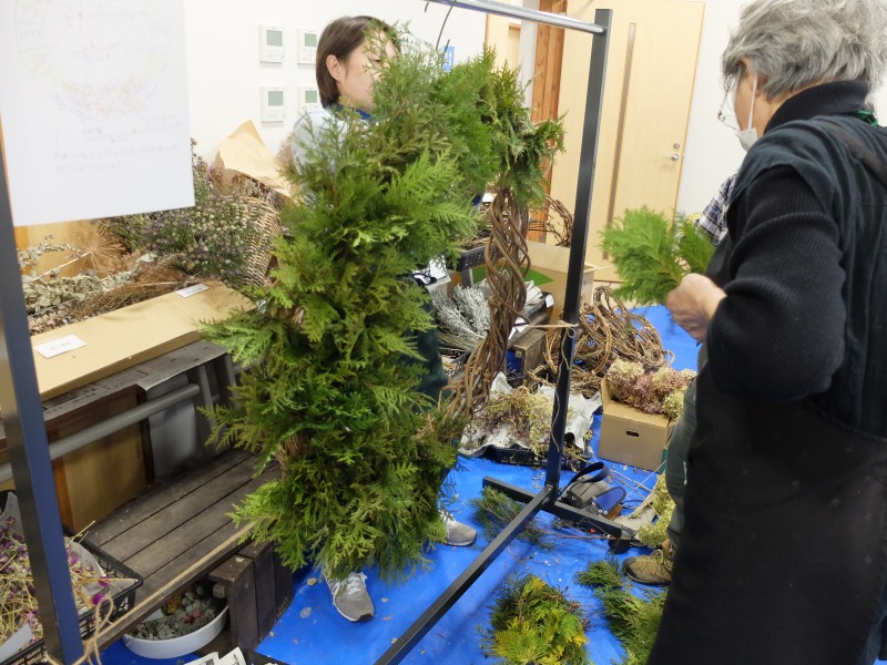 リース台にヒバのパーツを巻き付けている