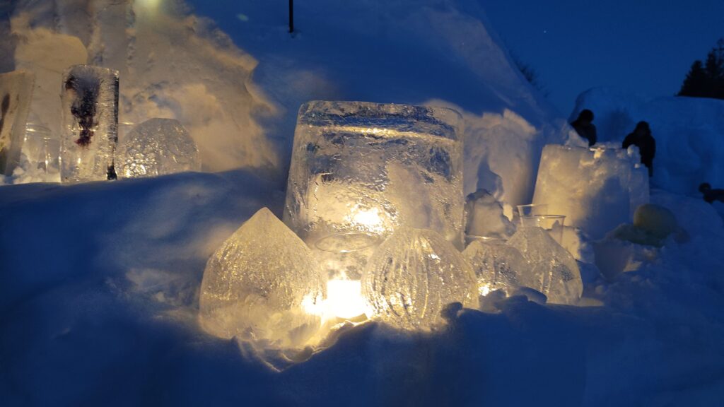 氷の中で灯るろうそくの灯の黄色と、背景の雪面が青く映ってい織る写真