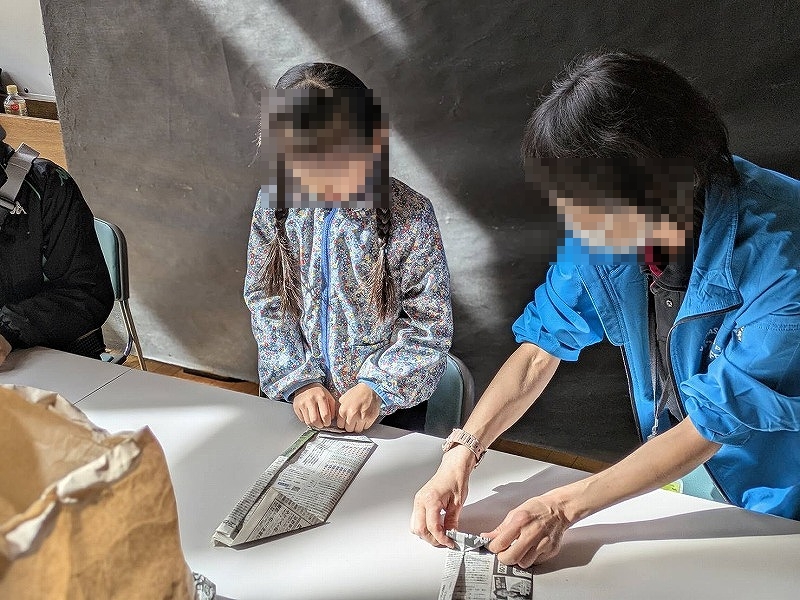 新聞紙を使った食器作りを子どもがレクチャーされている様子