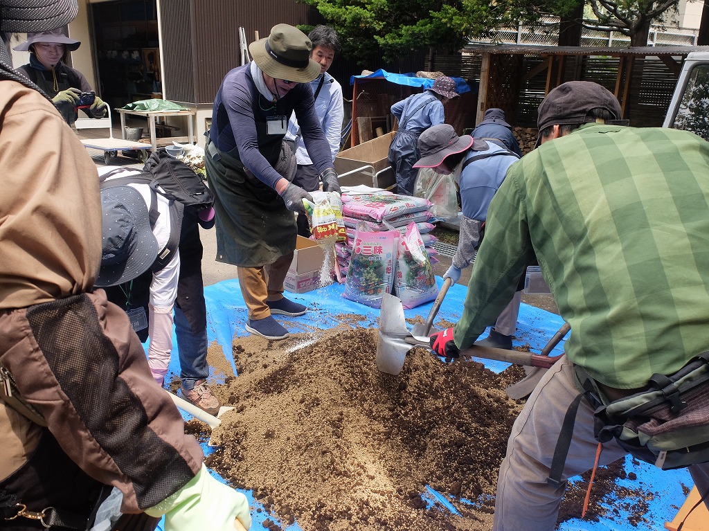 一人が用土の入った袋からブルーシートの上に土をあけてスコップを使って4名の受講者たちでで土を混ぜている様子