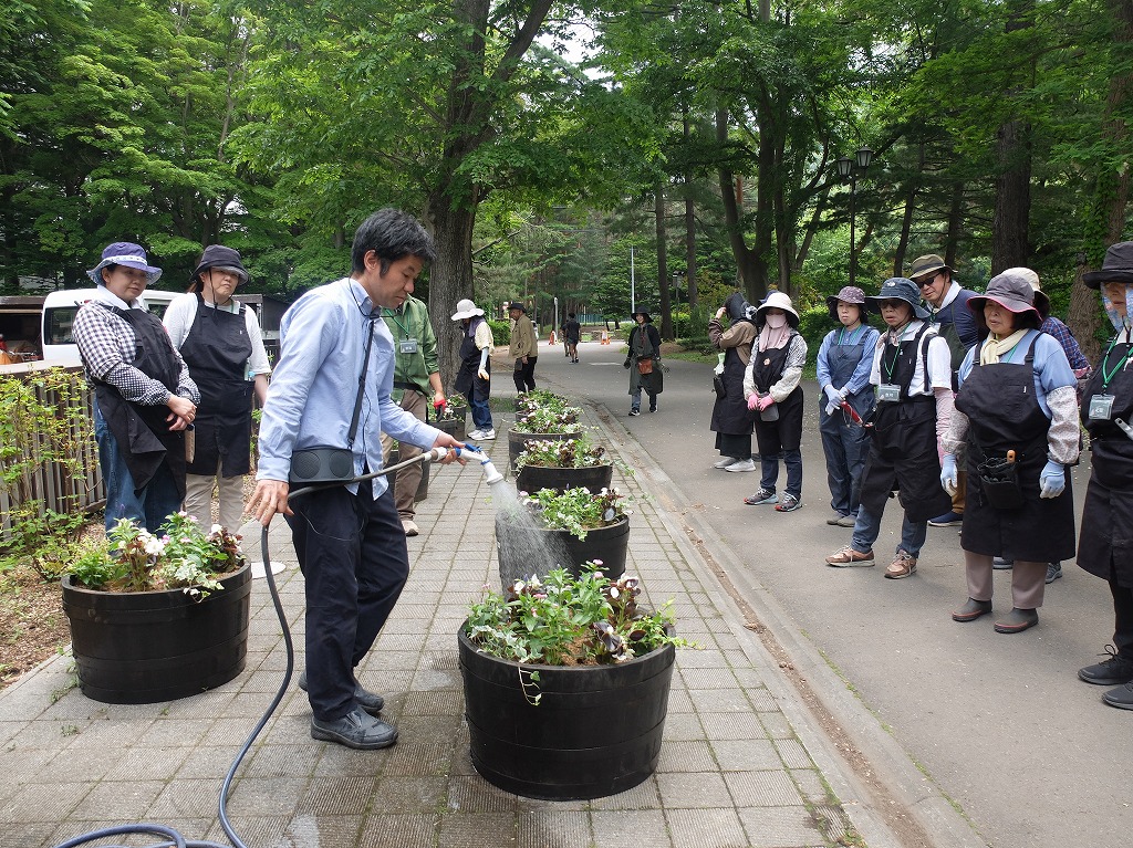 植込みが完成したコンテナに水やりの仕方を説明する講師の様子
