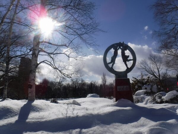 輝く太陽と、青空に向かって伸びゆく二人の子供の彫刻