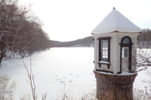 氷と雪に閉ざされた池と赤い屋根に雪が積もった取水塔