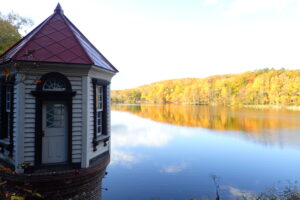 紅葉した木が映り込む池と赤い屋根の取水塔