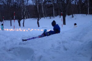 スノーキャンドルを背景にそり滑りする子供