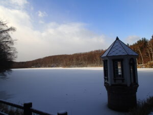 屋根に雪をかぶった取水塔と氷と雪に覆われた池