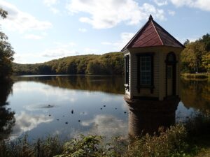 空の雲が映った池と赤い屋根の取水塔