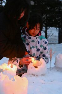 スノーキャンドルの外側の雪灯籠をの中に入れたろうそくに火をつける子ども