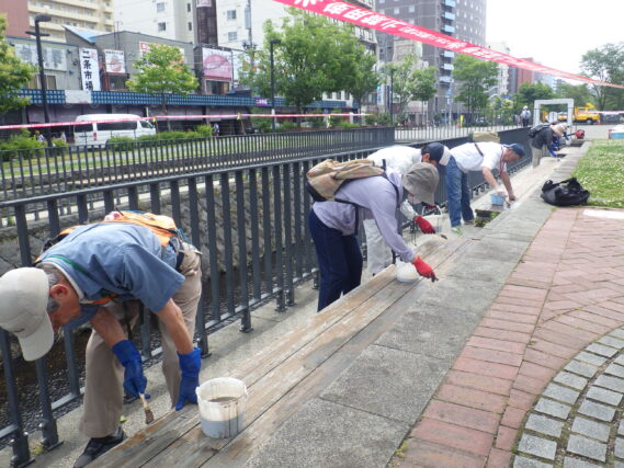 7月3日に狸二条広場の北側のベンチの塗装作業をするお助け隊