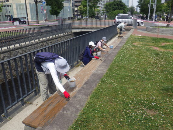 7月3日に狸二条広場の北側のベンチの塗装作業をするお助け隊