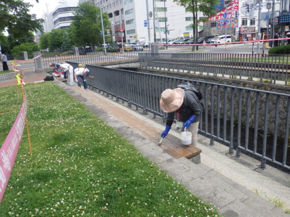 7月3日に狸二条広場の北側のベンチの塗装作業をするお助け隊