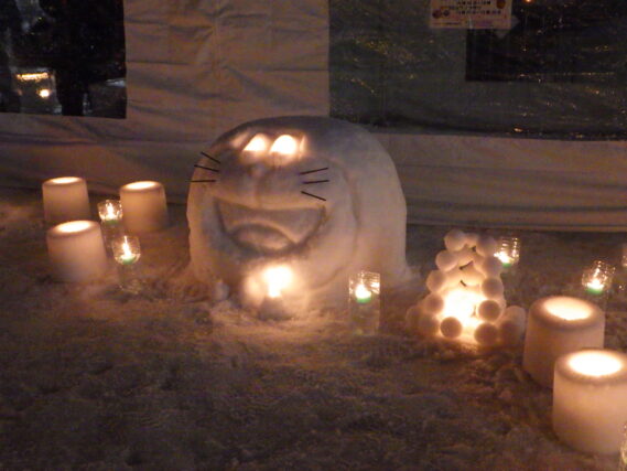 雪で作ったドラえもんの周りでスノーキャンドルが点灯されている様子