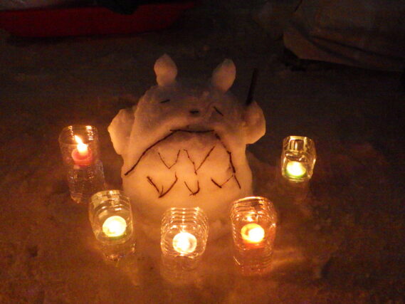 雪で作ったトトロの周りでスノーキャンドルが点灯されている様子