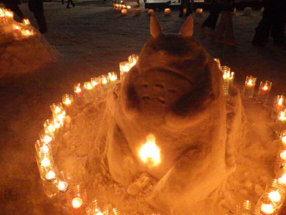 雪で作ったトトロの周りでスノーキャンドルが点灯されている様子