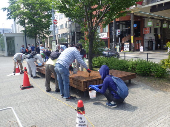 狸二条広場の縁台を塗装するお助け隊