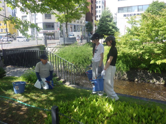 除草ボランティアから芝生のブタナなどの除草作業の指導を受ける高校生ボランティア