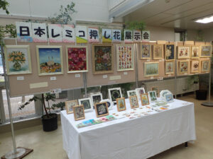 壁面に押し花で風景や鳥などを作った額の作品が並び、手前の机には小さな額の作品と葉が切作品が並ぶ。