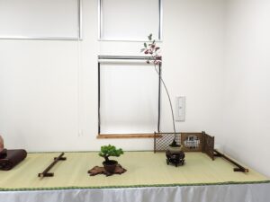 右手にスーッと茎が伸び上方に赤い実と赤に変化しつつある葉がついたカマツカの盆栽と添えのマツの小さな盆栽が並んだ一席