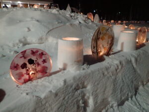 丸い円盤状の氷の中に花や葉が閉じ込められたアイスボードと雪を円筒状に固めたスノーキャンドルが並び、ろうそくの明かりが見える。